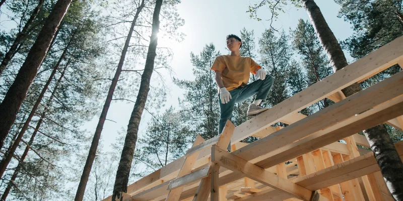 A carpenter on a wooden structure in a forest, engaged in construction work under the sun