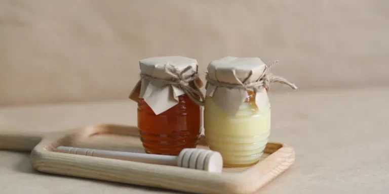 Two jars of honey on a wooden tray with a honey dipper