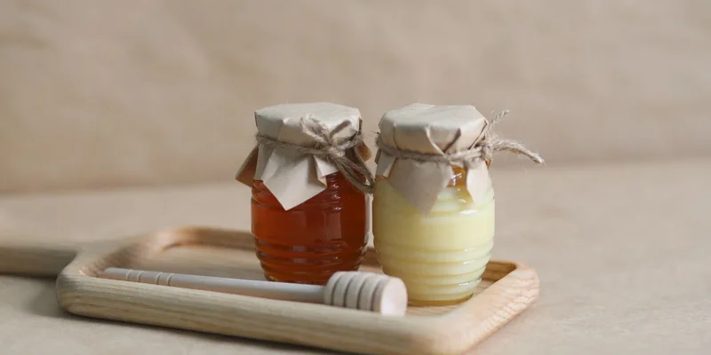 Two jars of honey on a wooden tray with a honey dipper