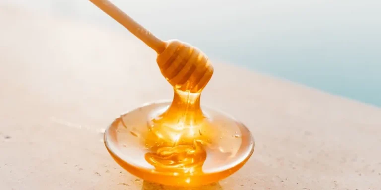 Golden honey flowing from a wooden dipper onto a glass plate, captured in warm daylight