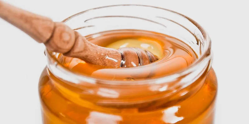 A detailed close-up of a wooden honey dipper in a jar filled with golden honey