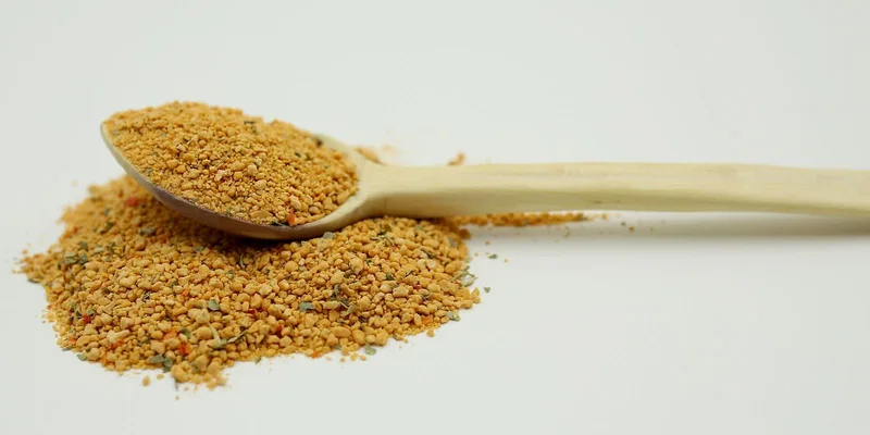 A wooden spoon filled with bee pollen granules on a white background