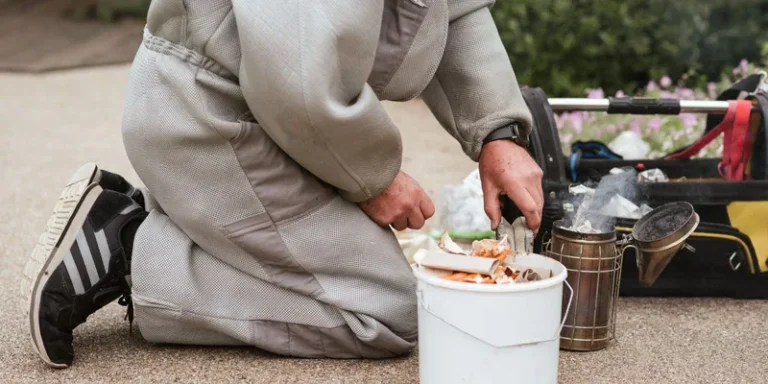 Beekeeper in protective suit preparing a bee smoker for hive management outdoors