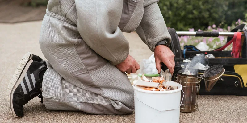 Beekeeper in protective suit preparing a bee smoker for hive management outdoors